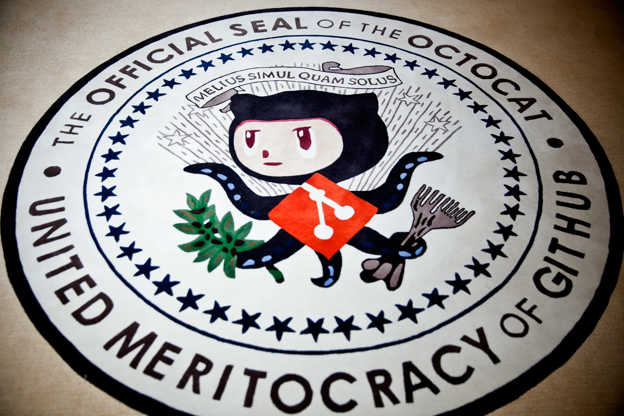 This photograph shows a seal on the floor of the GitHub headquarters. Octocat is emblazoned on the front. Text around the seal reads United Meritocracy of GitHub. The official seal of Octocat.